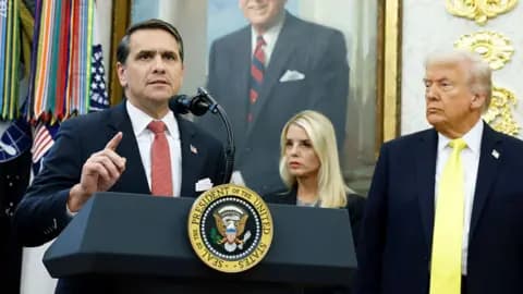 Todd Blance wears a blue suit and red tie as he speaks at a podium in the Oval Office with Donald Trump and Pam Bondi behind him.