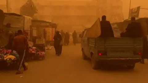 People and vehicles on a road that has turned orange because of a sandstorm