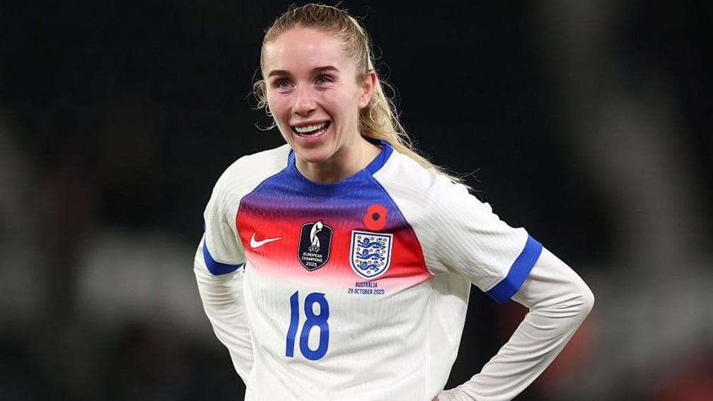 Missy Bo Kearns is wearing a white, red and blue England shirt and has her hands on her hips