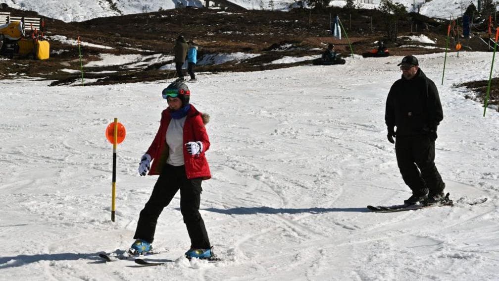 Two people ski down a snow-covered ski slope
