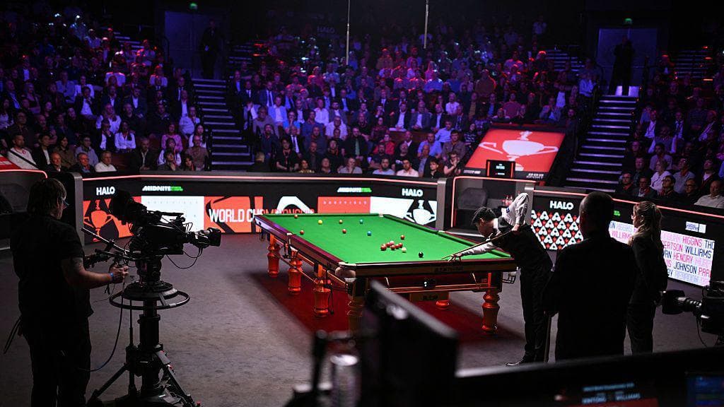 A view inside the Crucible during the 2025 World Championship final, with Zhao Xintong playing a shot at the table as a TV camera points towards him