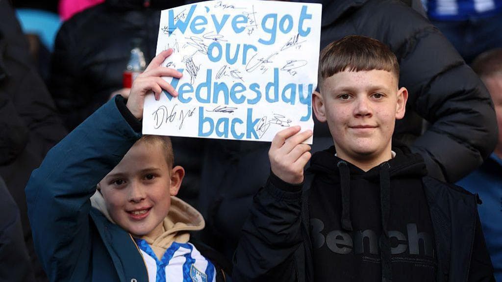 Two young Sheffield Wednesday fans hold a sign saying "We've got our Sheffield Wednesday back"