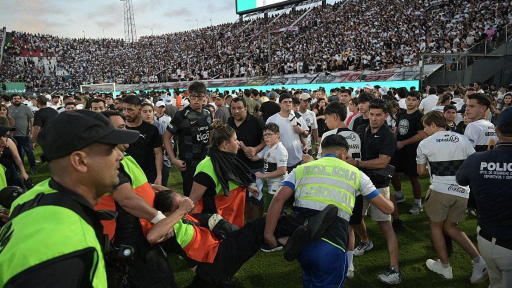 A police officer carries a fan of Cerro Porteno as they walk on the pitch after clashes with police officers