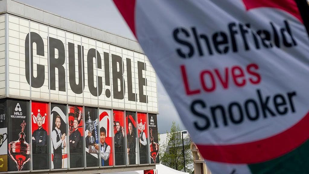 View of the Crucible theatre, with faces of past champions on the windows of the venue, and with a flag in the foreground with the words 'Sheffield Loves Snooker' on it.