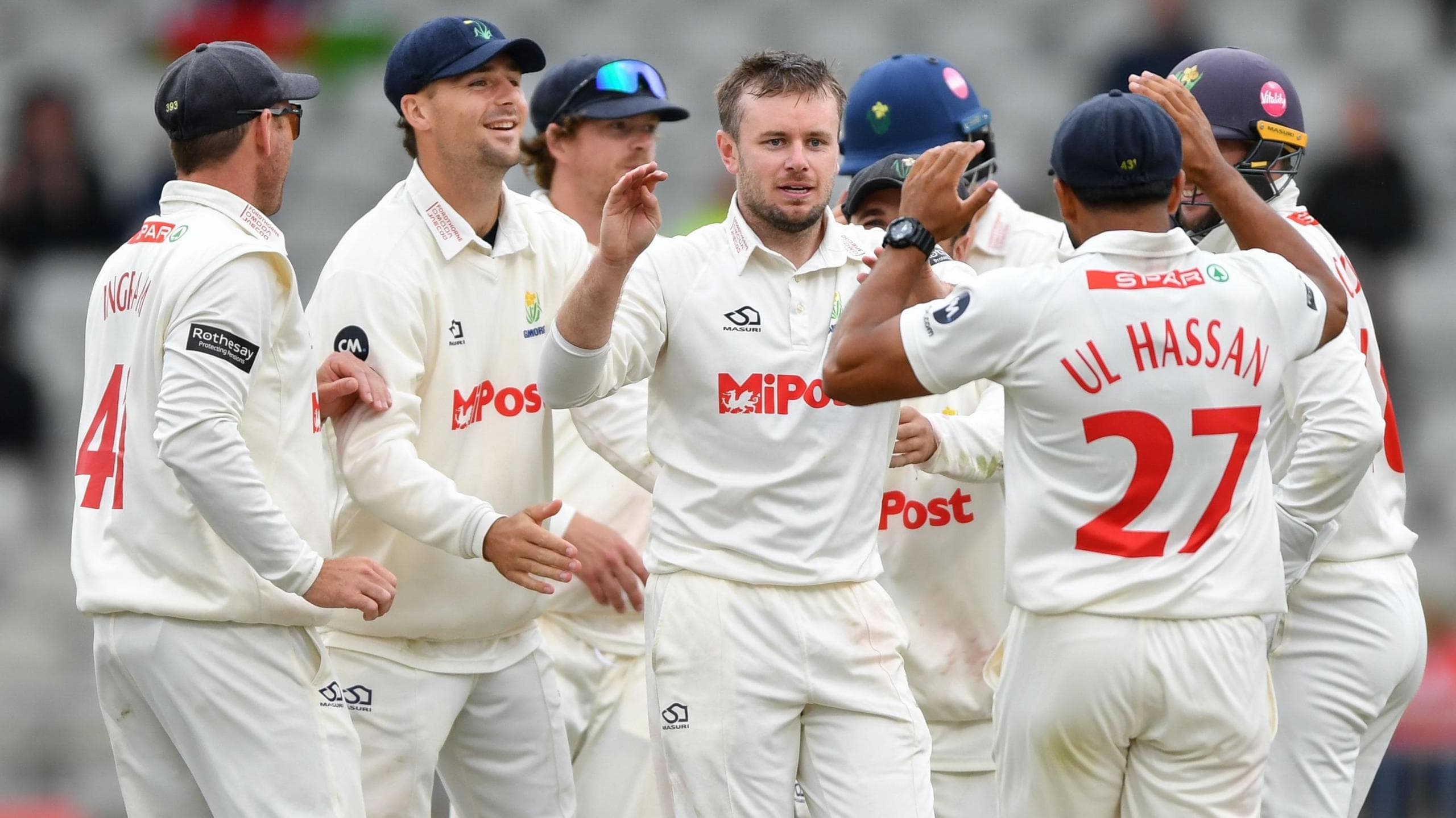 Mason Crane, with both hands raised, celebrates taking a wicket with his team-mates against Lancashire at Old Trafford in July 2025 as he prepares to high-five Zain ul Hassan