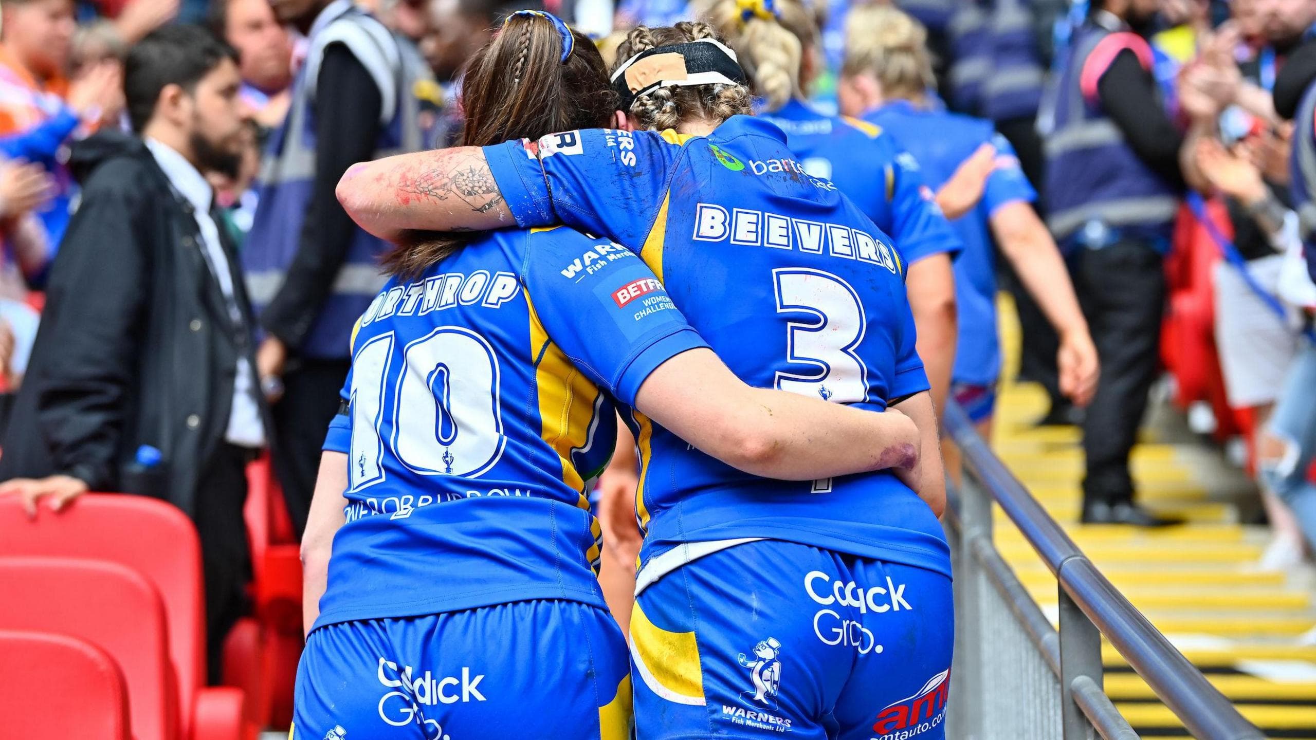 Izzy Northrop and Caitlin Beevers are joined arm in arm in embrace as they walk the Wembley steps to the Royal Box to receive their runners-up medals after the 2024 Challenge Cup final defeat by St Helens.