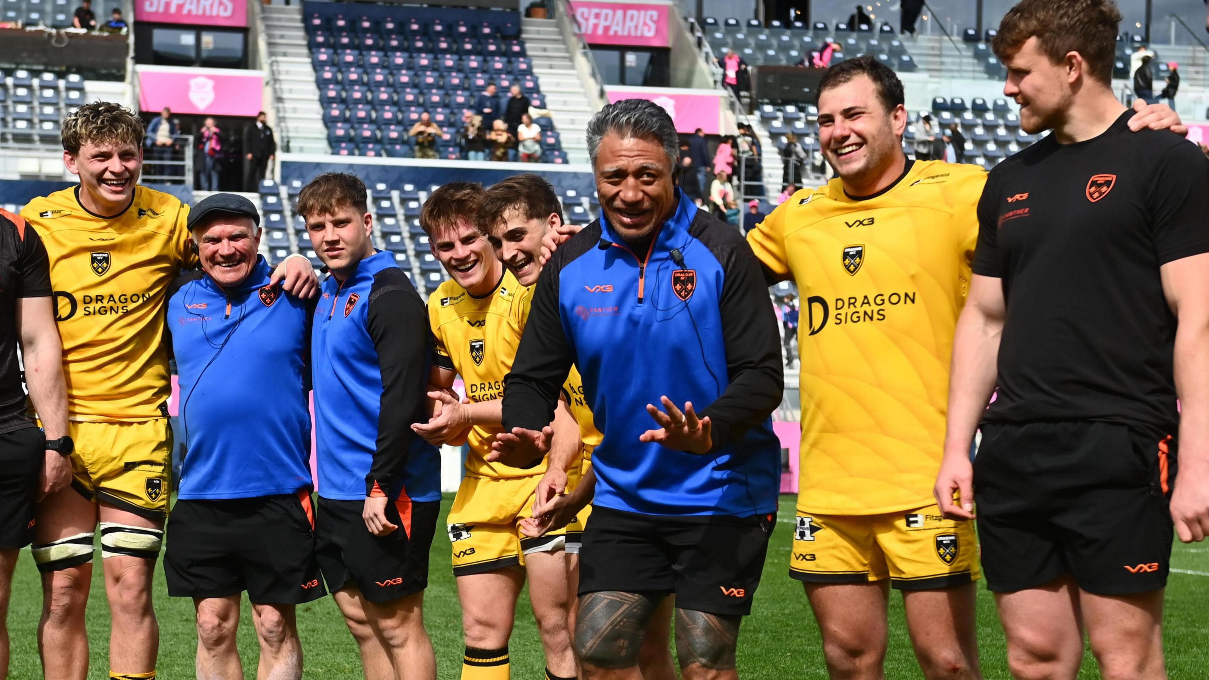 Filo Tiatia looks pleased and animated talking to smiling players on the pitch after the win in Paris
