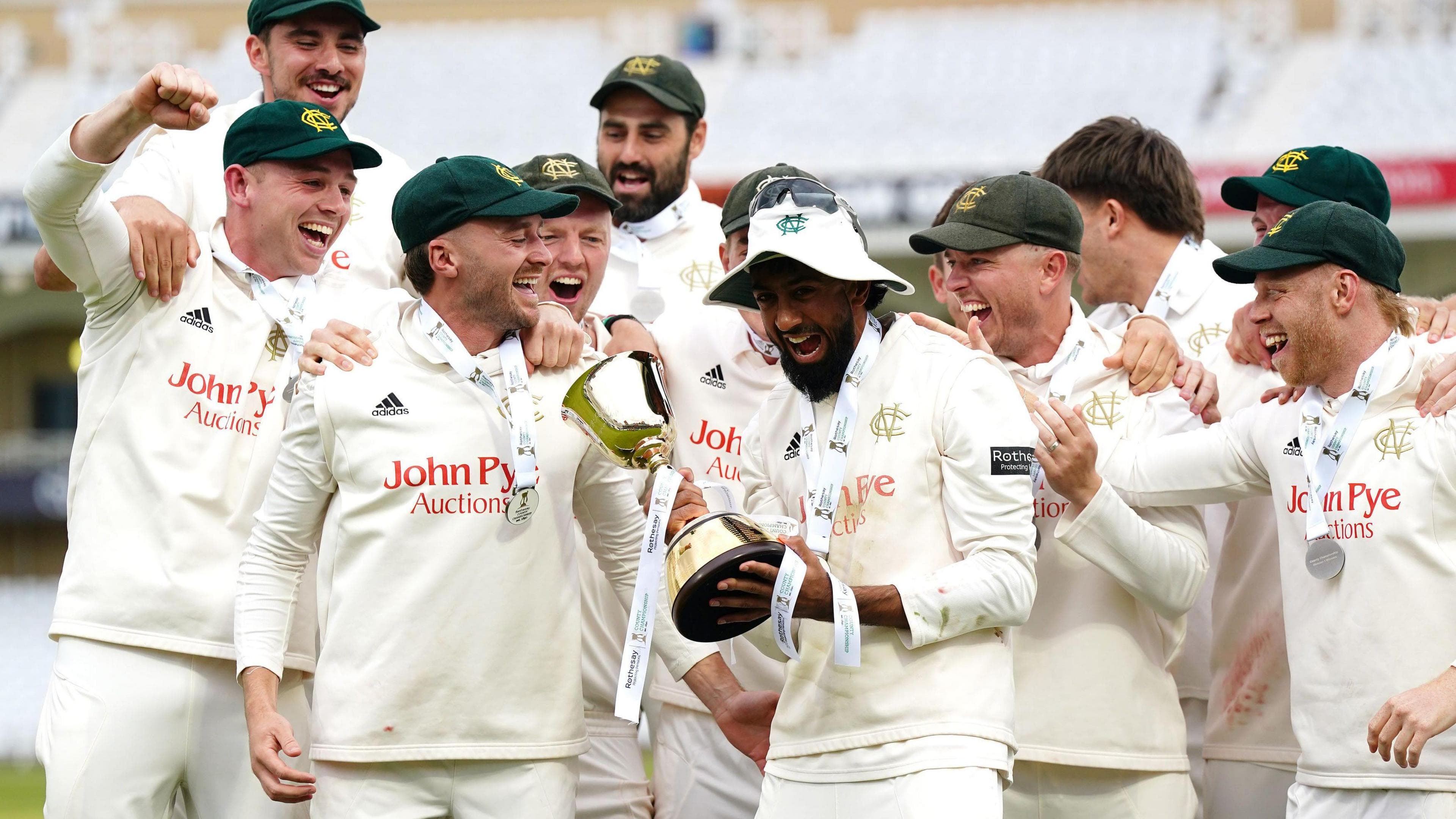 Nottinghamshire captain Haseeb Hameed holds the Division One trophy in both hands with a big smile on his face as the rest of his Nottinghamshire team-mates celebrate alongside him