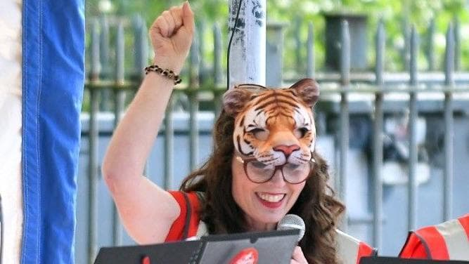 A woman with a tiger face mask on smiles and sings at a charity event