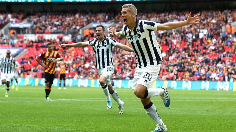 Steve Morison celebrates, running with his arms outstretched along the touchline of the pitch at Wembley Stadium, with players running behind him to congratulate him